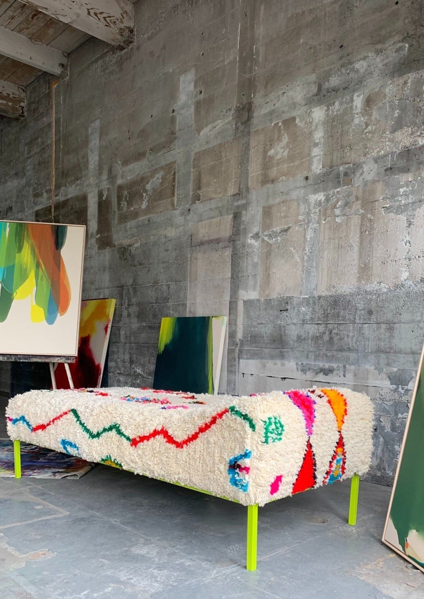 day bed is set up in urban art studio amongst many paintings that highlight colors.