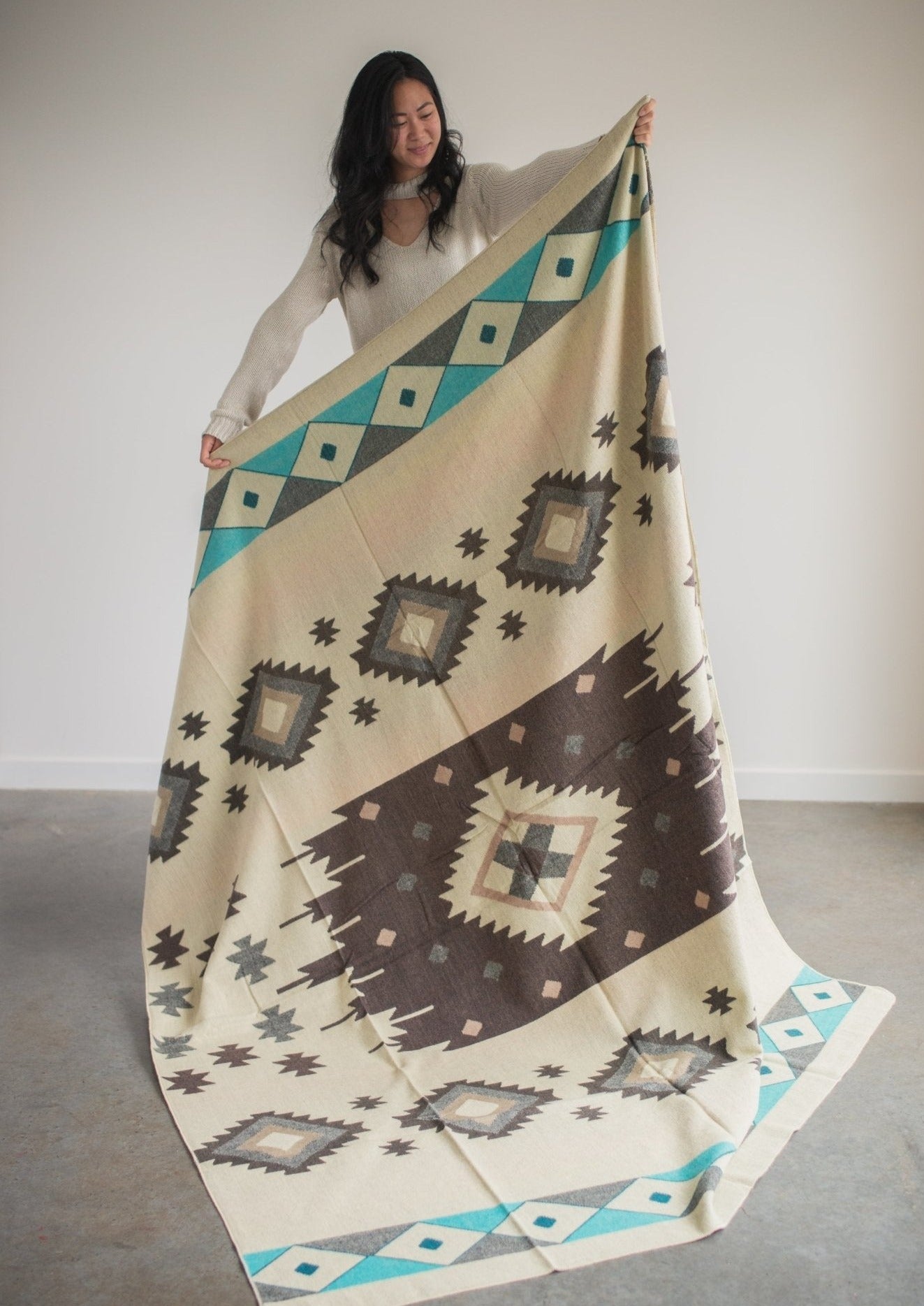 Asian girl wearing cozy sweater holds up reverse side of alpaca blanket to display full design.