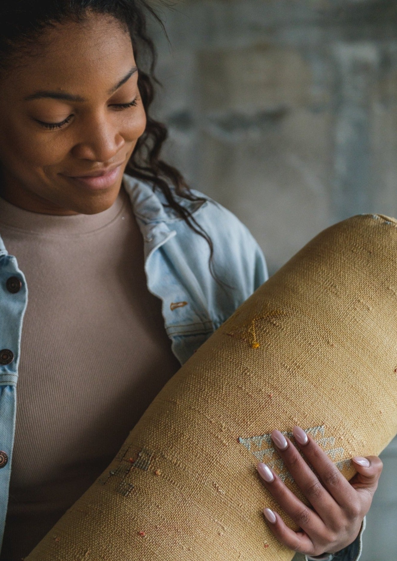 close up saffron lumber pillow made from vegan friendly material in morocco with hand stitched berber symbols. long pearl nails hold pillow by beautiful African American model 