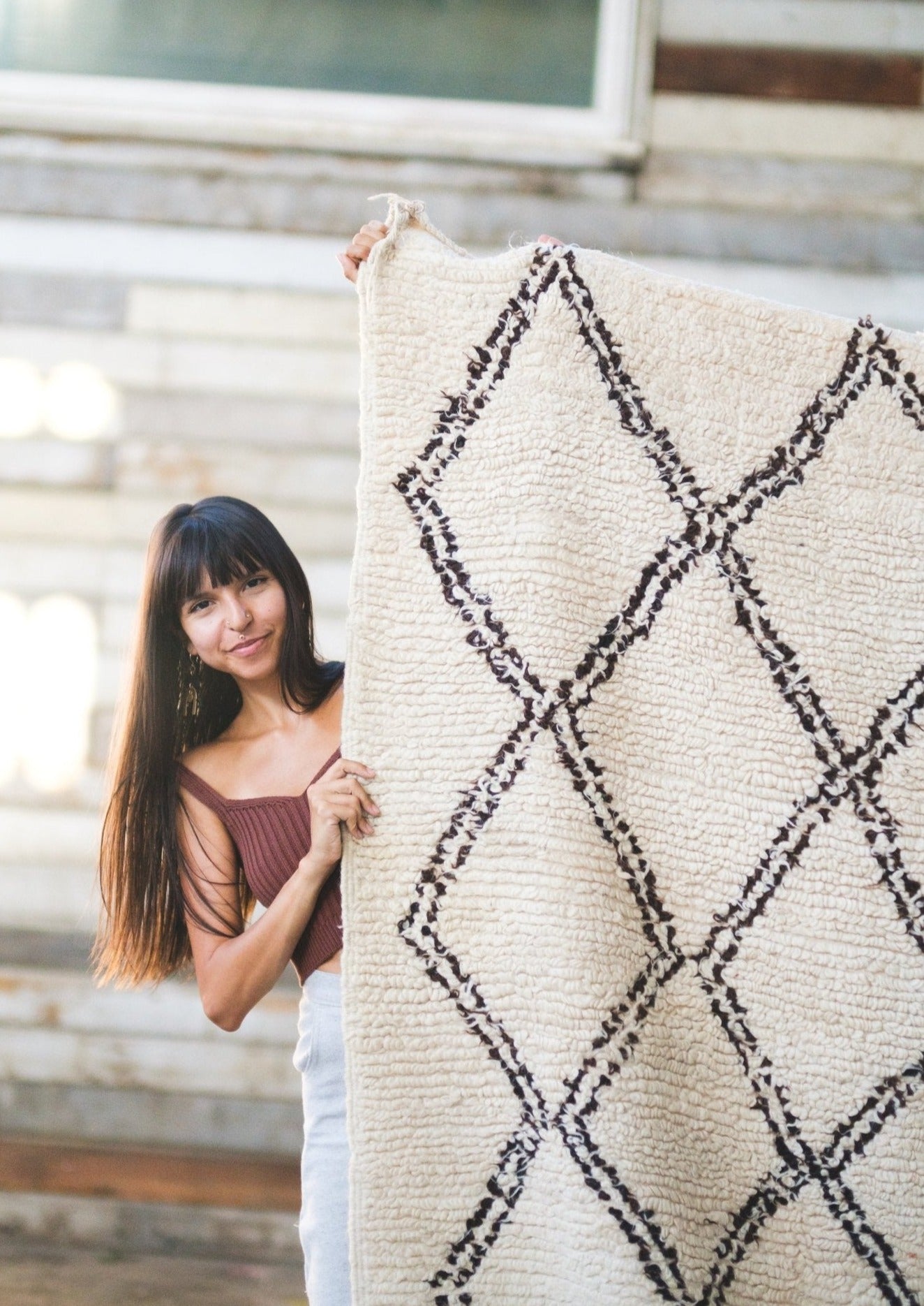cute smiling girl peers around a beni ourain moroccan rug with sunlight hitting her long brown hair. 