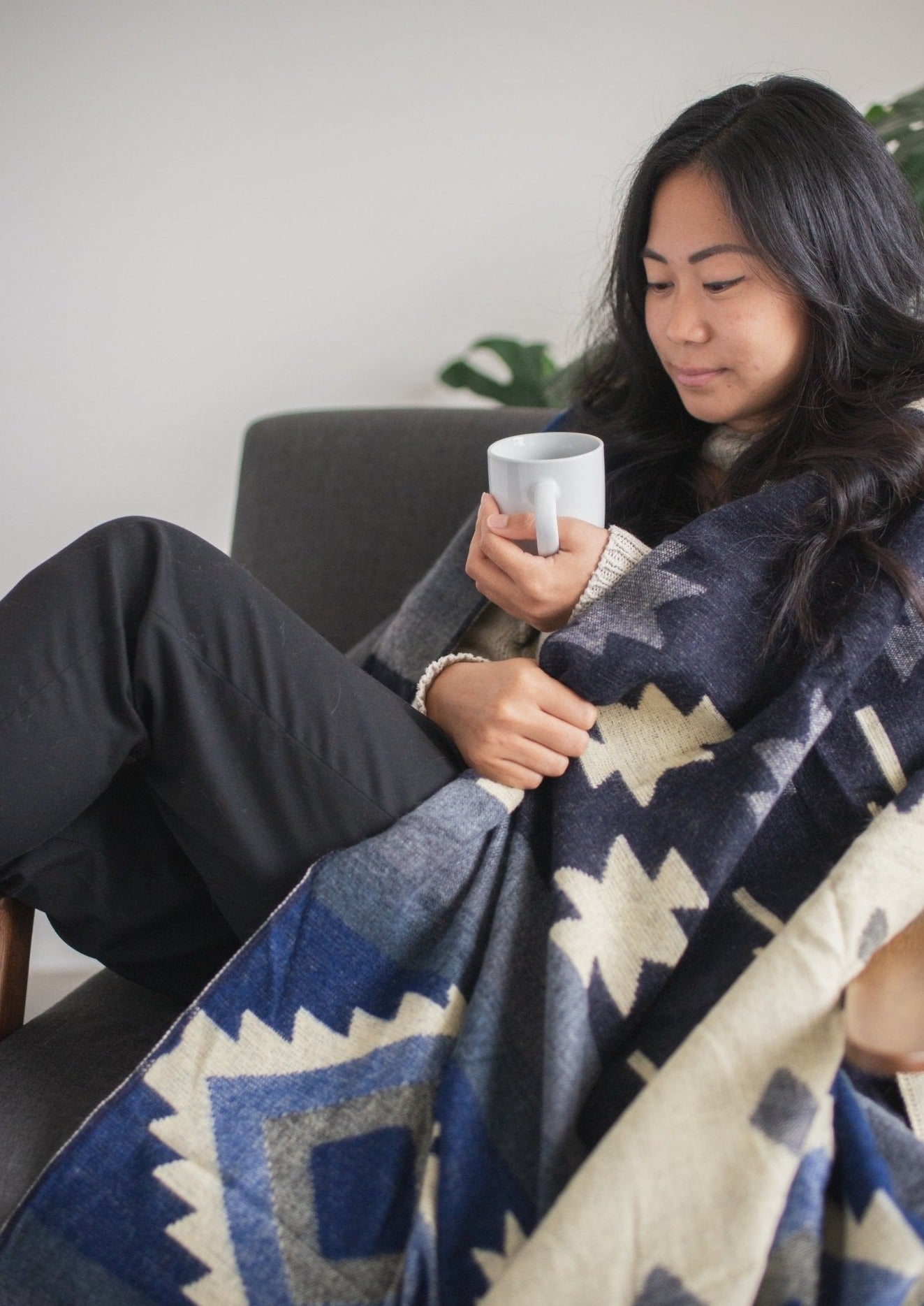 asian girl wraps up in her alpaca first thing in the morning with her cup of coffee. Her apartment is sophisticated