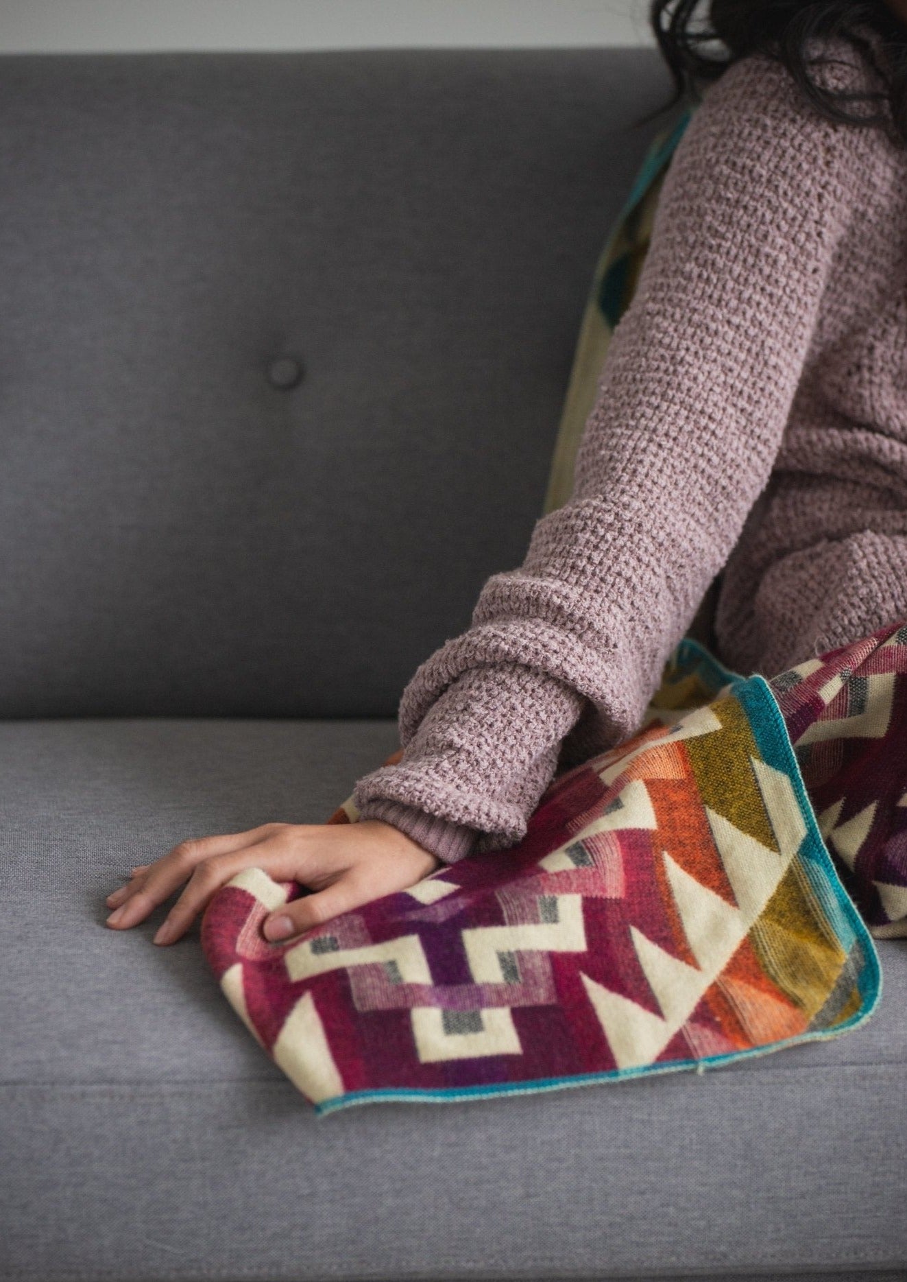 detail of alpaca blanket. asian girl is resting her hand on the soft material while wearing a cozy sweatshirt on the sofa 