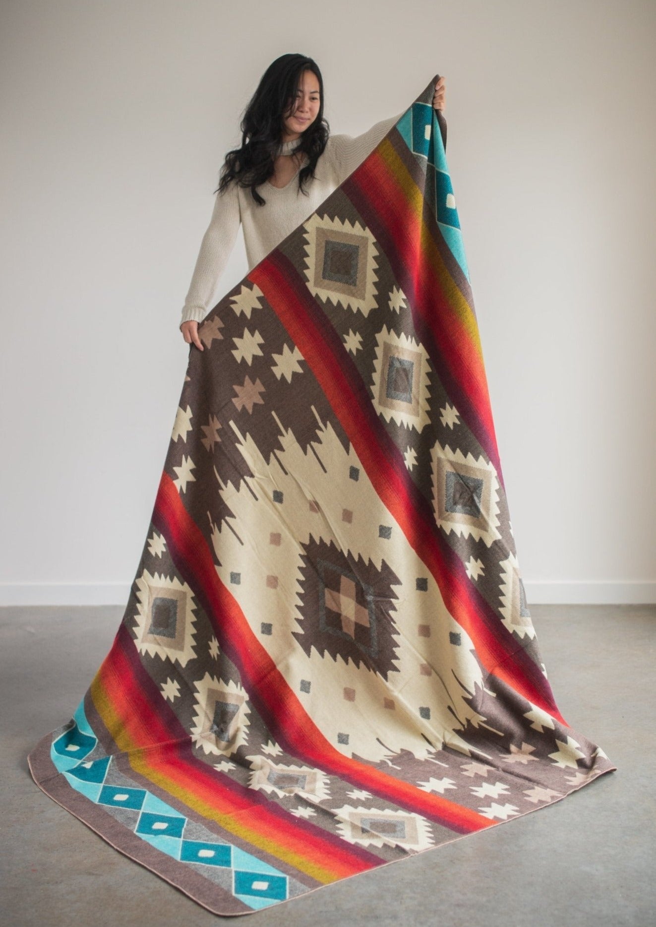 Asian girl wearing a cozy sweater holds up a red alpaca blanket to display full design 